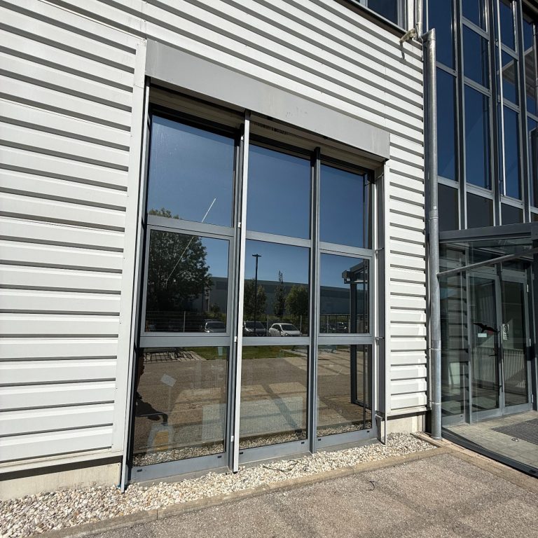 Sonnenschutz Glasgeregelter Eingang mit grauem Rahmen an einer modernen Gebäudefassade.