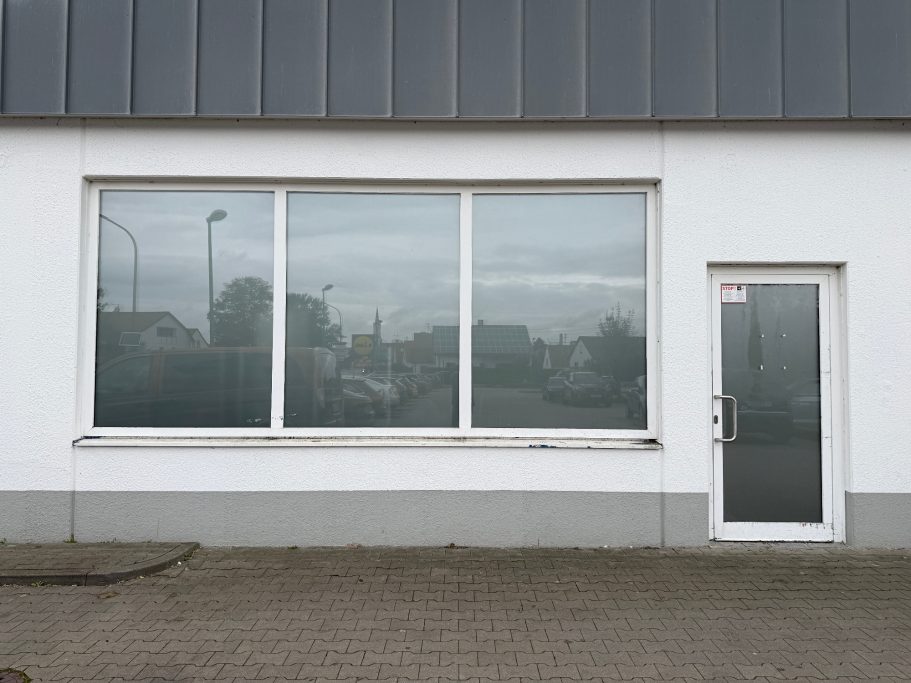 Fensterfront eines modernen Gebäudes mit grauem Dach und Tür an der rechten Seite.