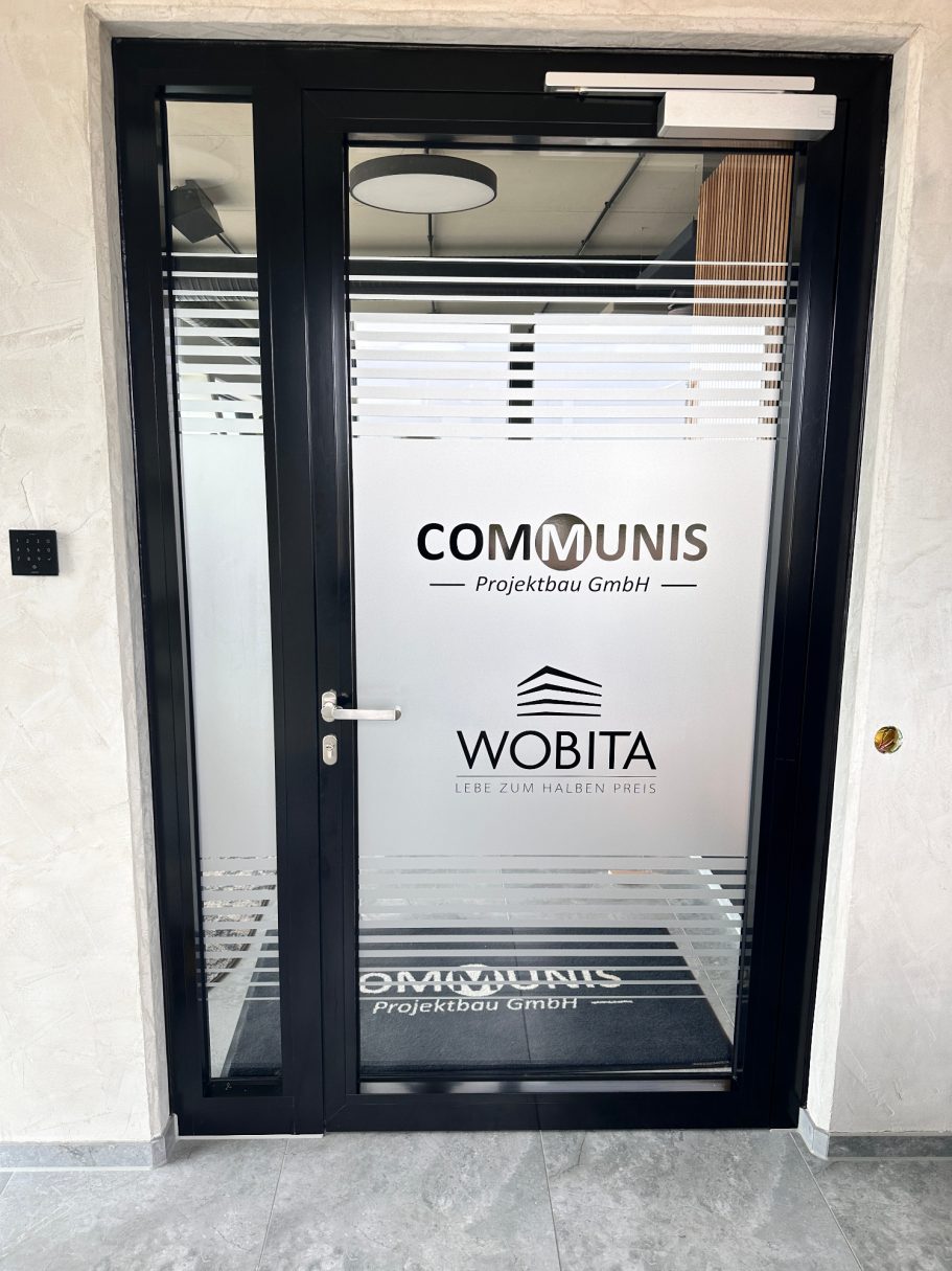 Glas-Eingangstür mit Aufschriften von COMUNIS und WOBITA. Transparente Fensterverkleidung.