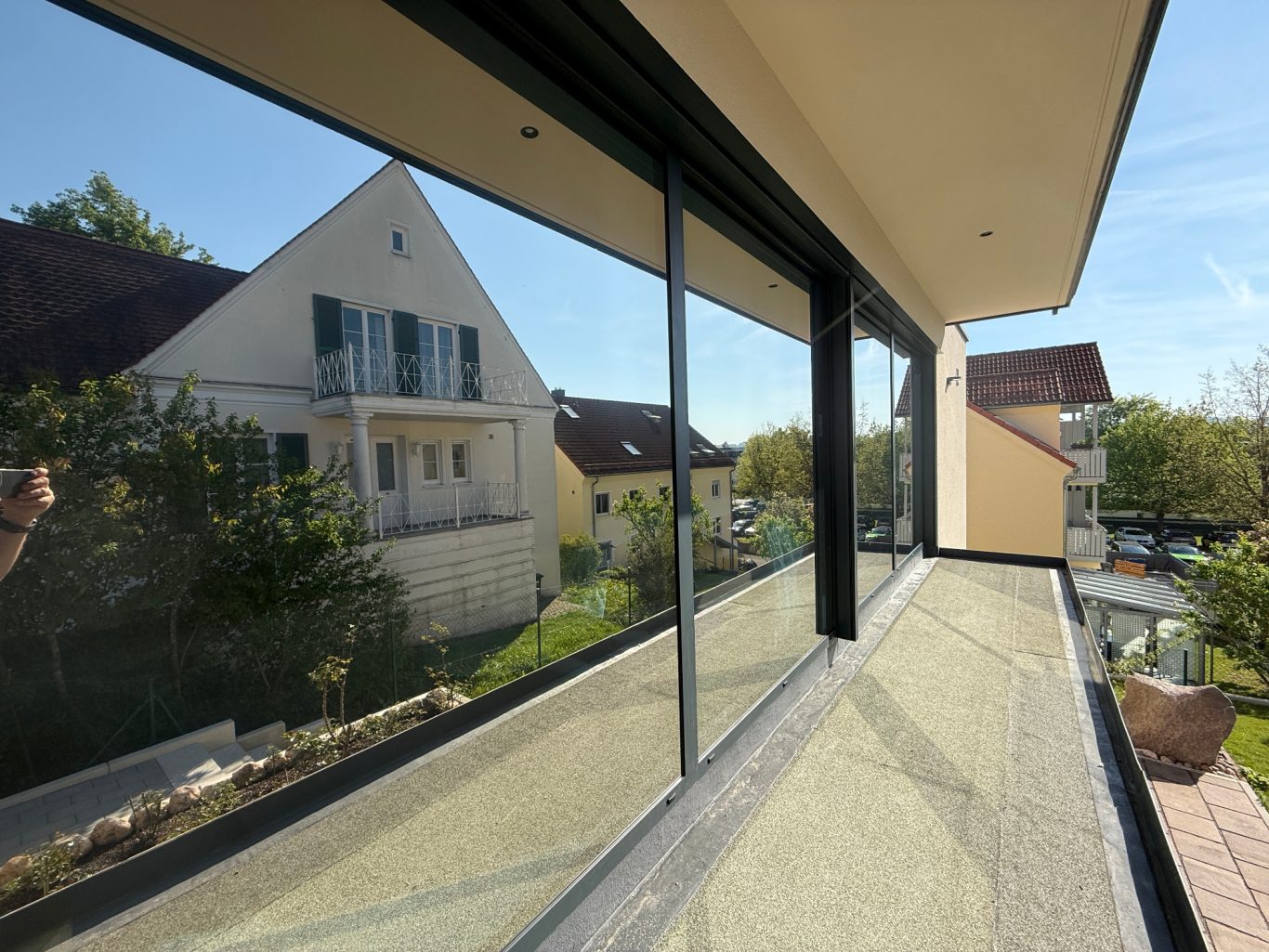 Balkon mit Blick auf ein Wohnhaus und grünen Garten im sonnigen Wetter.