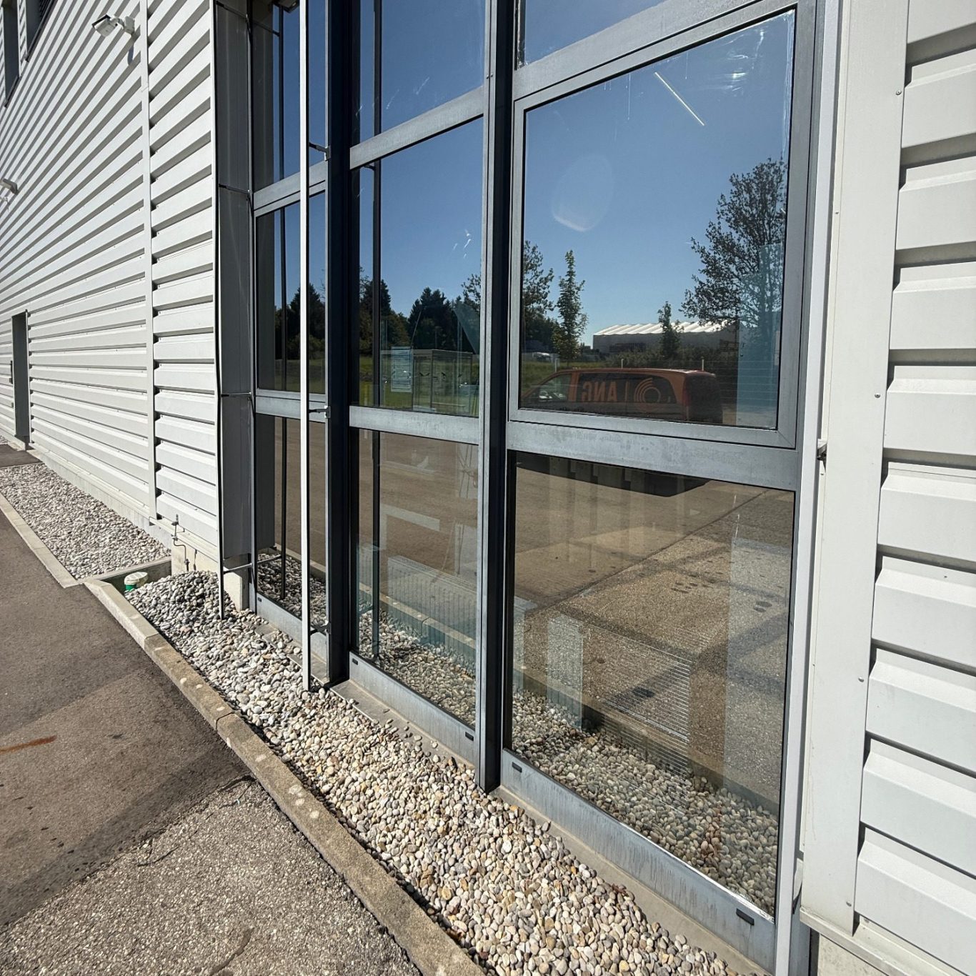 Sonnenschutz Fensterfront eines modernen Gebäudes mit Kiesbett und gepflastertem Boden.