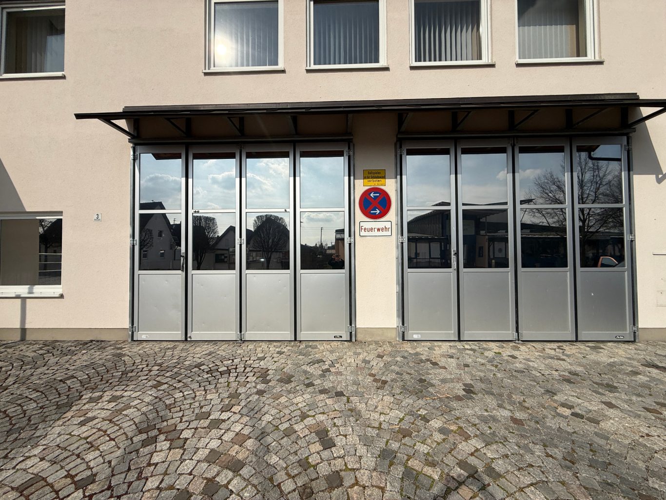 Moderne Fassade mit großen Fenstern und einem Parkplatzschild in der Nähe.