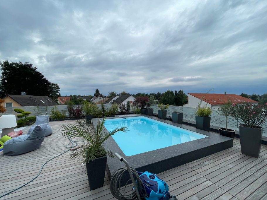 Moderne Dachterrasse mit Pool, Pflanzen und Blick auf die Umgebung unter bewölktem Himmel.