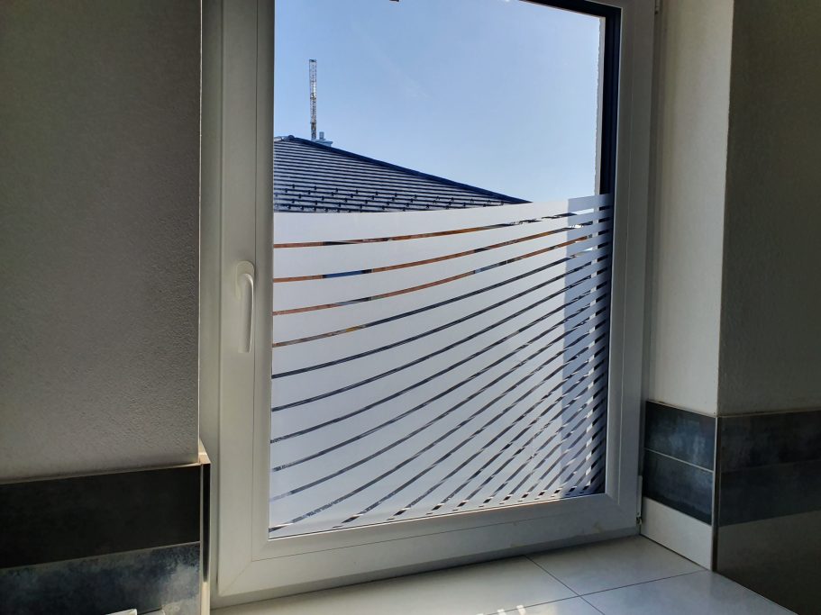 Fenster mit Jalousien, Blick auf ein Dach und einen blauen Himmel.