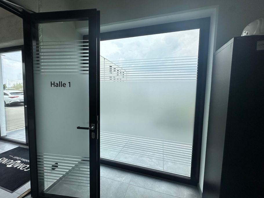 Tür mit frosted Glas führt zu einem hellen Raum mit großen Fenstern.